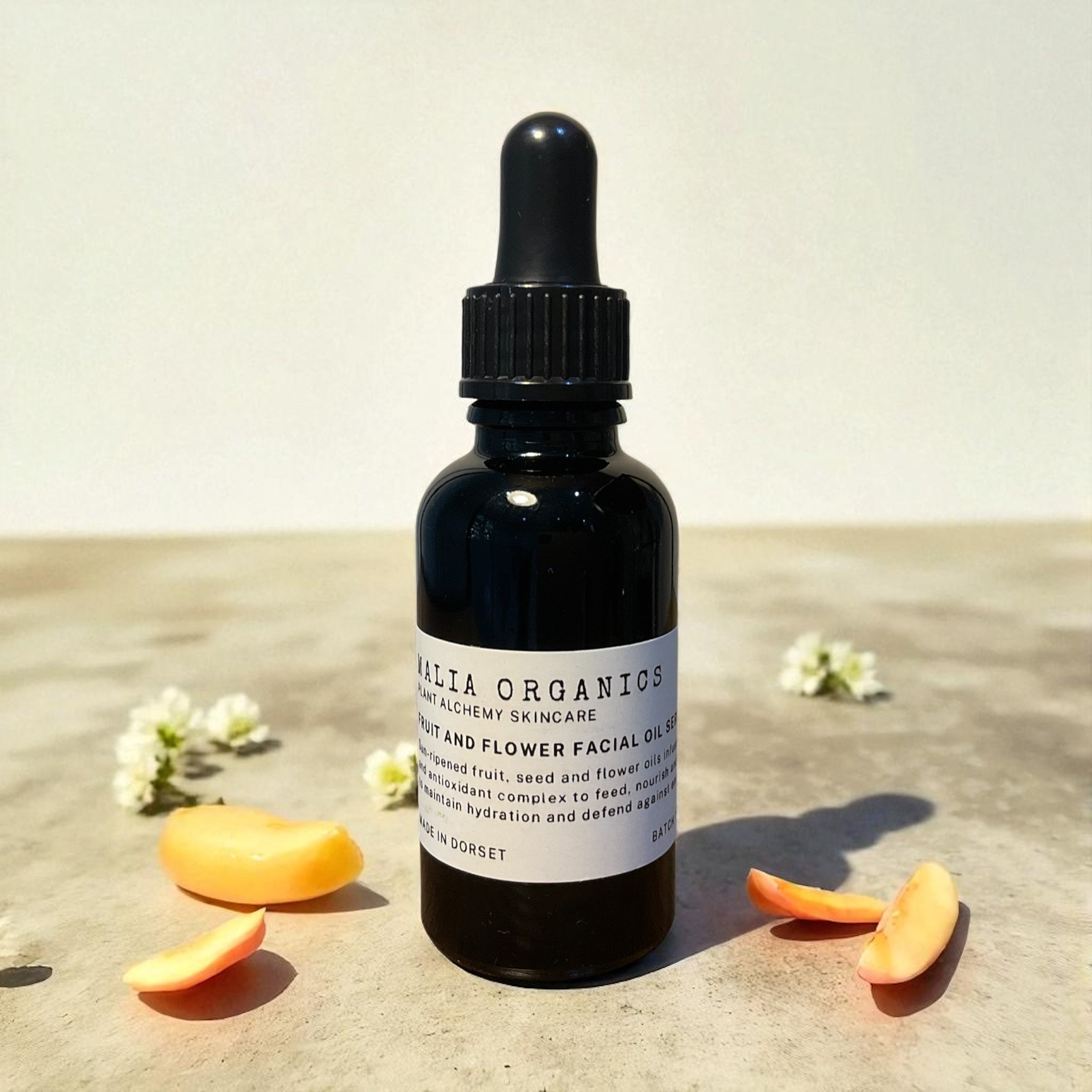 Black dropper bottle with a label on a light surface with orange slices and white flowers.