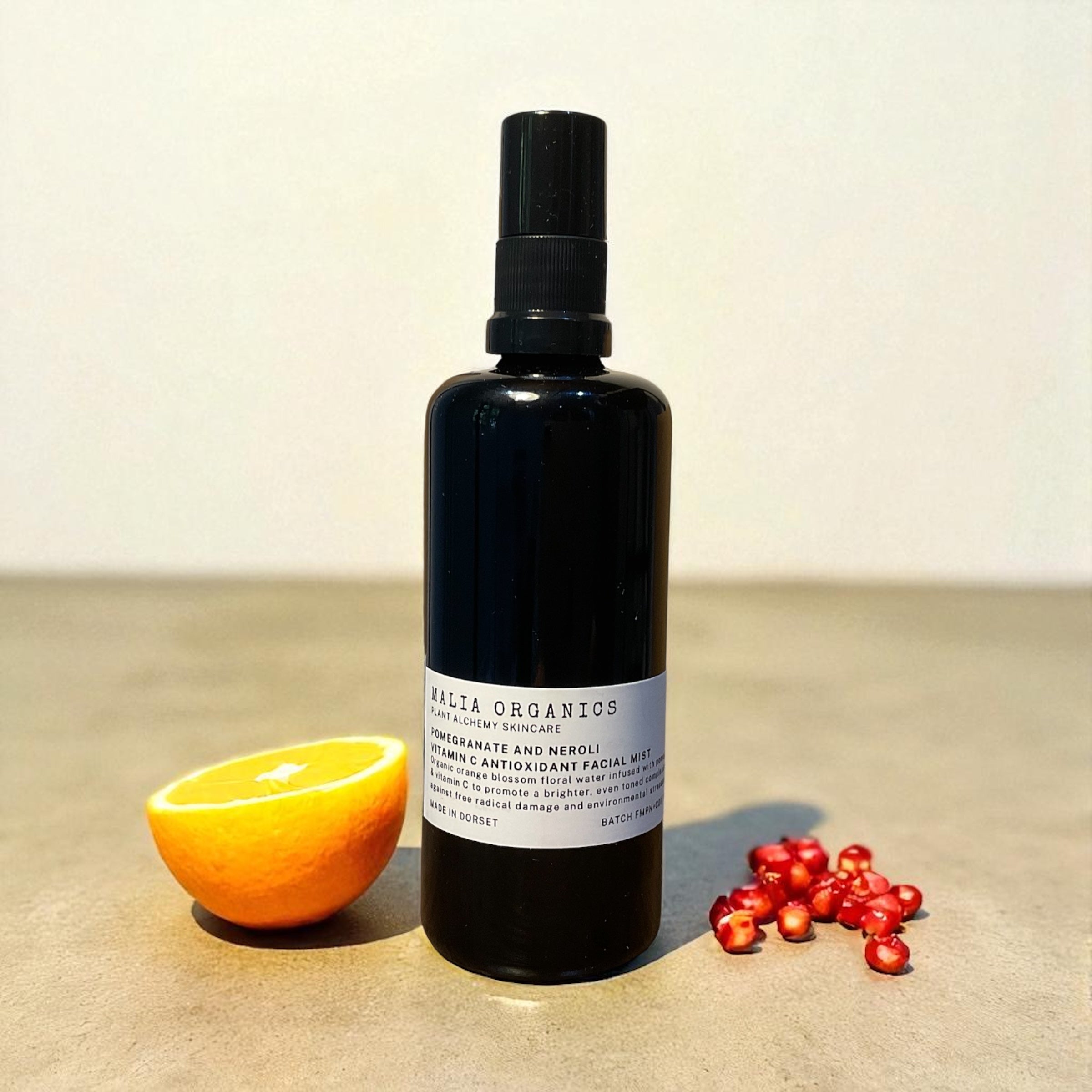 Black bottle with a label next to an orange and berries on a beige surface